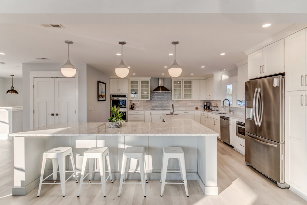 This is an example of a large beach style l-shaped open plan kitchen in Wilmington with an undermount sink, shaker cabinets, grey cabinets, quartz benchtops, grey splashback, porcelain splashback, stainless steel appliances, laminate floors, with island, multi-coloured floor and white benchtop.