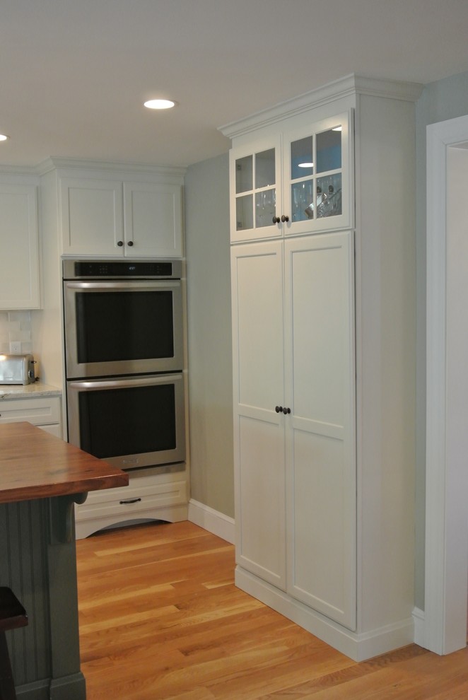 Inspiration for a transitional galley light wood floor eat-in kitchen remodel in Boston with an undermount sink, shaker cabinets, white cabinets, wood countertops, white backsplash, ceramic backsplash, stainless steel appliances, an island and brown countertops