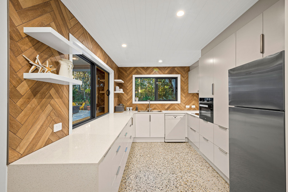 Mid-sized contemporary galley separate kitchen in Other with a drop-in sink, white cabinets, quartz benchtops, stainless steel appliances, concrete floors, timber, porcelain splashback, flat-panel cabinets, brown splashback, no island, brown floor and beige benchtop.