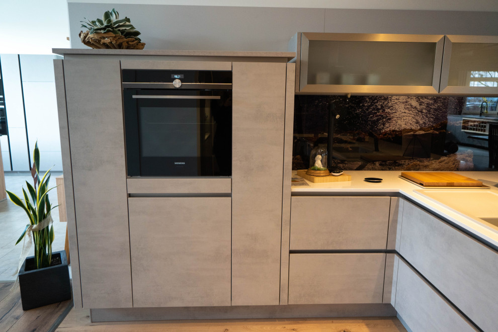 Foto de cocina gris y negra actual con puertas de armario grises, encimera de cuarzo compacto, electrodomésticos negros, suelo laminado, suelo beige y encimeras blancas