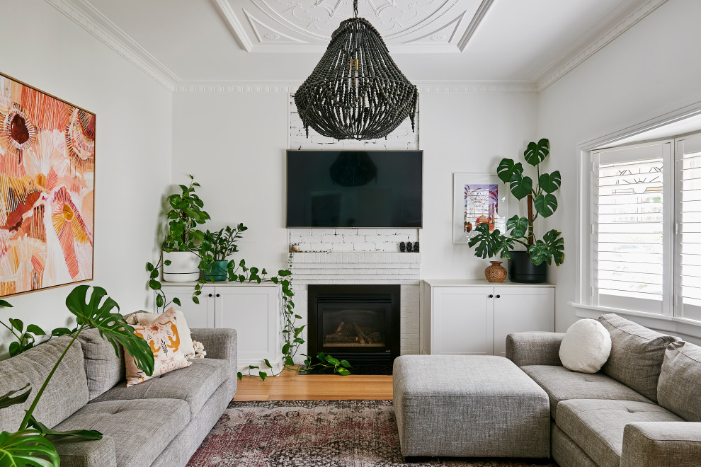 This is an example of a medium sized contemporary formal open plan living room in Geelong with white walls, light hardwood flooring, a standard fireplace, a brick fireplace surround and a wall mounted tv.