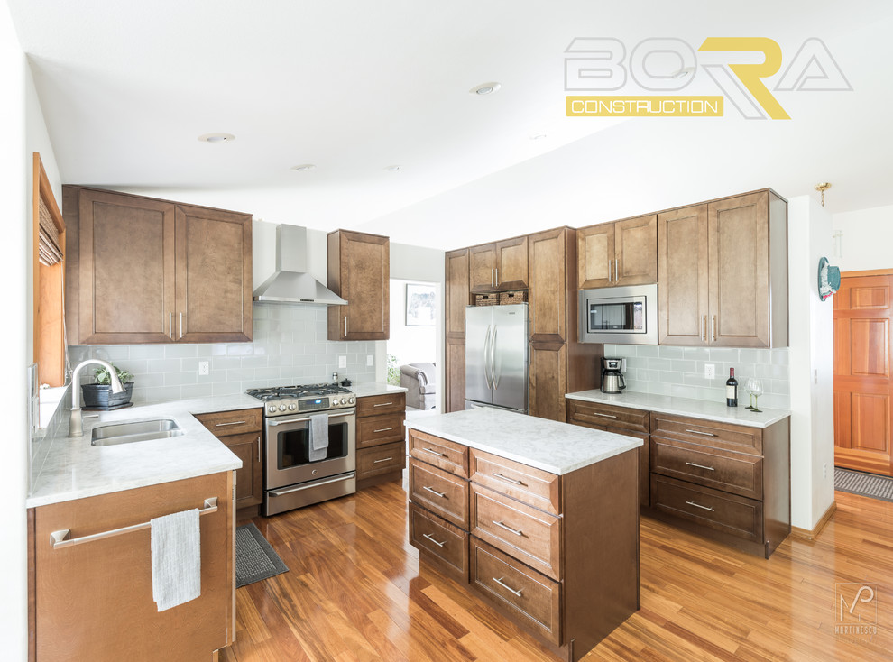 Inspiration for a mid-sized transitional l-shaped medium tone wood floor and brown floor eat-in kitchen remodel with an undermount sink, shaker cabinets, medium tone wood cabinets, quartz countertops, gray backsplash, ceramic backsplash, stainless steel appliances and an island