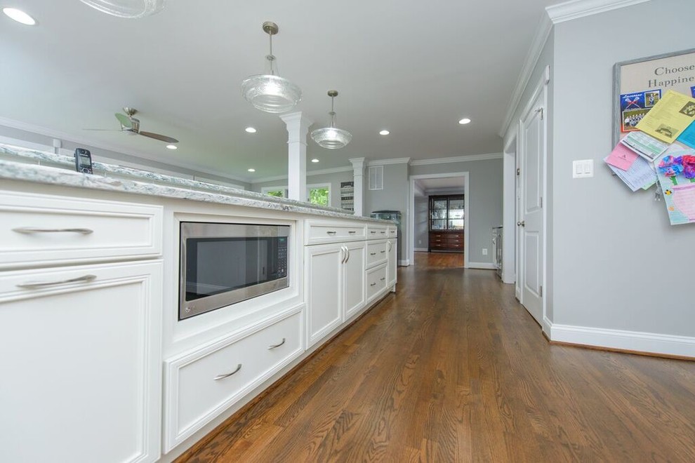 Inspiration for a transitional l-shaped medium tone wood floor eat-in kitchen remodel in Baltimore with a farmhouse sink, beaded inset cabinets, white cabinets, granite countertops, gray backsplash, glass tile backsplash, stainless steel appliances and an island