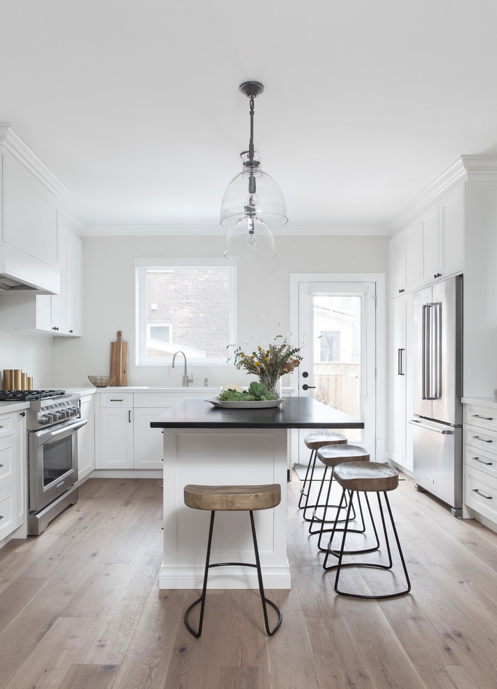 Kitchen pantry - small transitional l-shaped light wood floor and brown floor kitchen pantry idea in Toronto with a double-bowl sink, recessed-panel cabinets, white cabinets, soapstone countertops, white backsplash, porcelain backsplash, stainless steel appliances, an island and black countertops