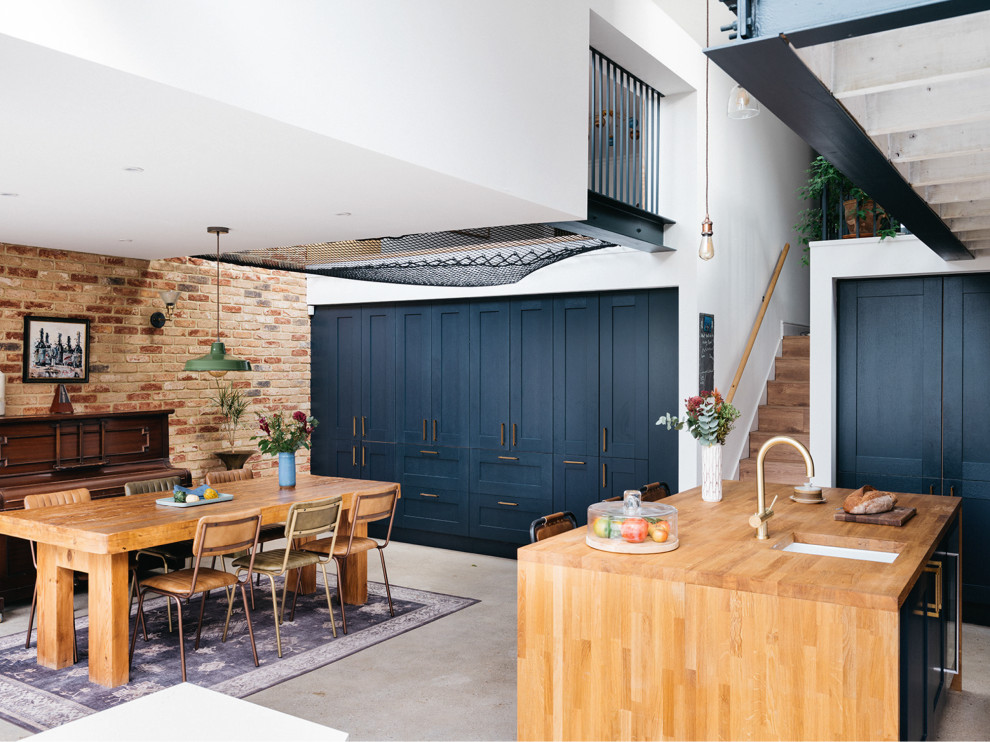 Inspiration for a large contemporary l-shaped open plan kitchen in London with an undermount sink, shaker cabinets, blue cabinets, wood benchtops, yellow splashback, ceramic splashback, black appliances, concrete floors, with island, grey floor, white benchtop and vaulted.