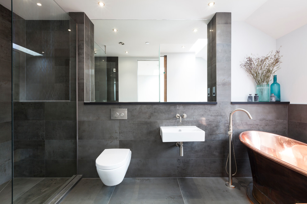 Inspiration for a contemporary bathroom in London with a wall-mount sink, a freestanding tub, an alcove shower, a wall-mount toilet, gray tile and white walls.