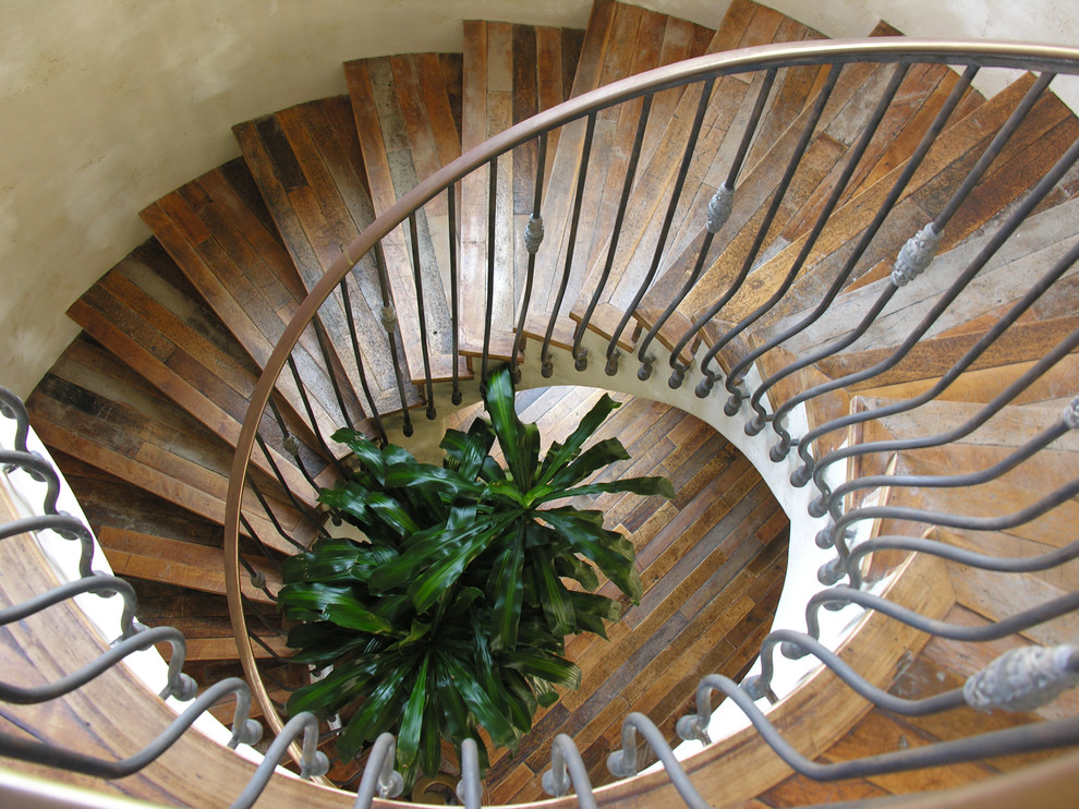 Photo of a large arts and crafts wood spiral staircase in San Diego with wood risers and metal railing.