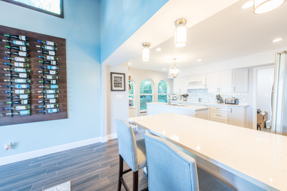 Large transitional u-shaped porcelain tile and brown floor eat-in kitchen photo with an undermount sink, shaker cabinets, white cabinets, quartz countertops, white backsplash, marble backsplash, stainless steel appliances and two islands