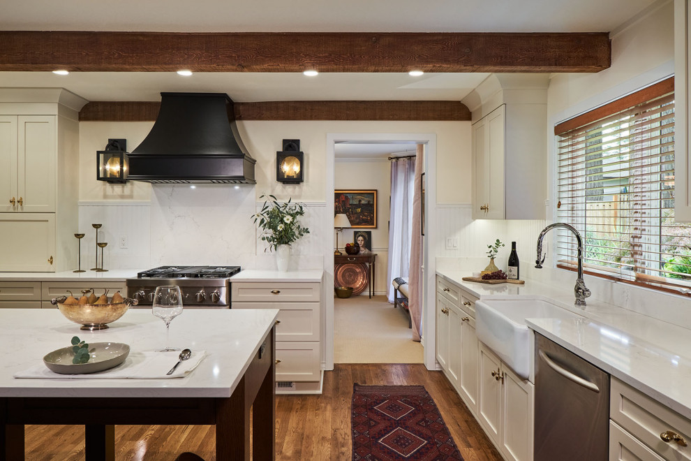 This is an example of a large traditional u-shaped separate kitchen in Portland with a farmhouse sink, shaker cabinets, beige cabinets, quartz benchtops, white splashback, timber splashback, stainless steel appliances, medium hardwood floors, with island, brown floor, white benchtop and exposed beam.