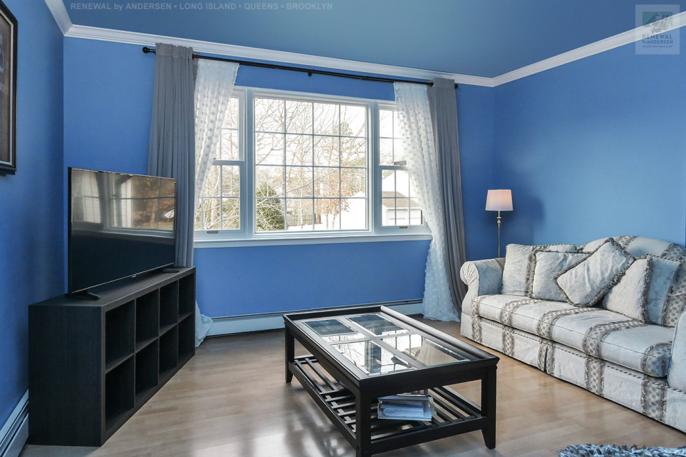 Bild på ett stort allrum med öppen planlösning, med ett finrum, blå väggar, ljust trägolv, en fristående TV och beiget golv