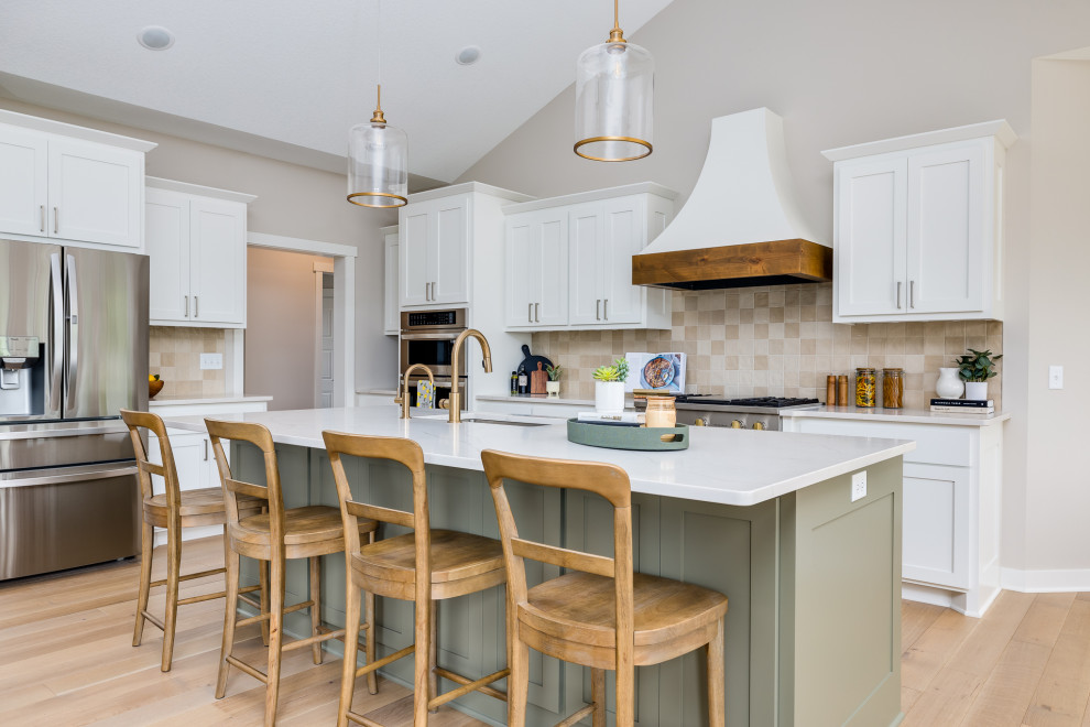 Photo of a large transitional l-shaped open plan kitchen in Other with a single-bowl sink, shaker cabinets, white cabinets, quartz benchtops, beige splashback, ceramic splashback, stainless steel appliances, medium hardwood floors, with island, beige floor, white benchtop and vaulted.
