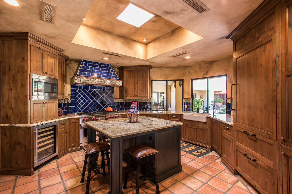 Inspiration for an u-shaped kitchen in Phoenix with a farmhouse sink, shaker cabinets, medium wood cabinets, blue splashback, ceramic splashback, stainless steel appliances, terra-cotta floors, with island, red floor and beige benchtop.