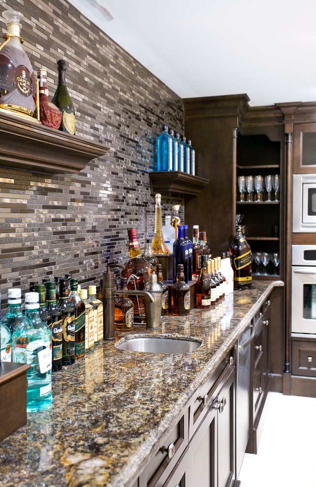 Photo of a large transitional single-wall wet bar in Toronto with an undermount sink, shaker cabinets, granite benchtops, black splashback, glass tile splashback, limestone floors, beige floor, dark wood cabinets and multi-coloured benchtop.