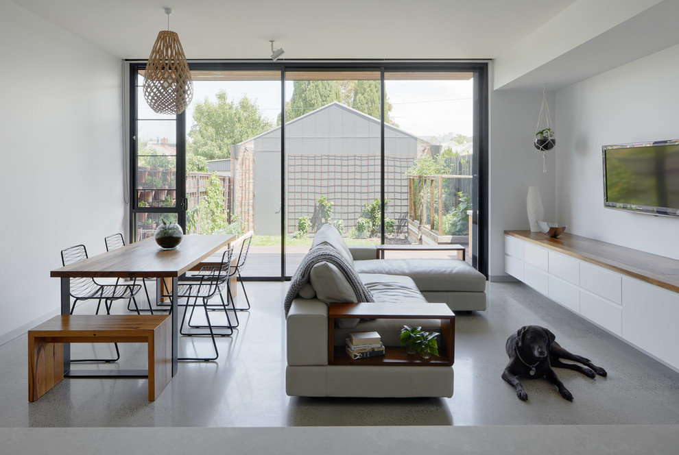 Small contemporary open concept living room in Melbourne with white walls, concrete floors, a wall-mounted tv and grey floor.