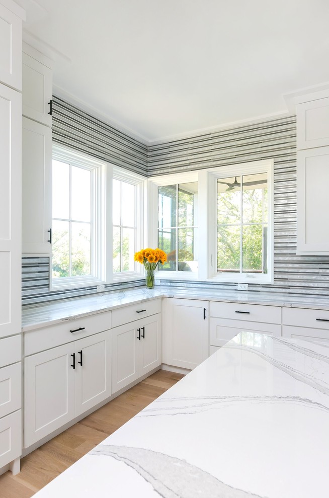 Large minimalist l-shaped light wood floor and beige floor eat-in kitchen photo in Portland with a single-bowl sink, shaker cabinets, white cabinets, quartz countertops, gray backsplash, mosaic tile backsplash, stainless steel appliances, an island and white countertops