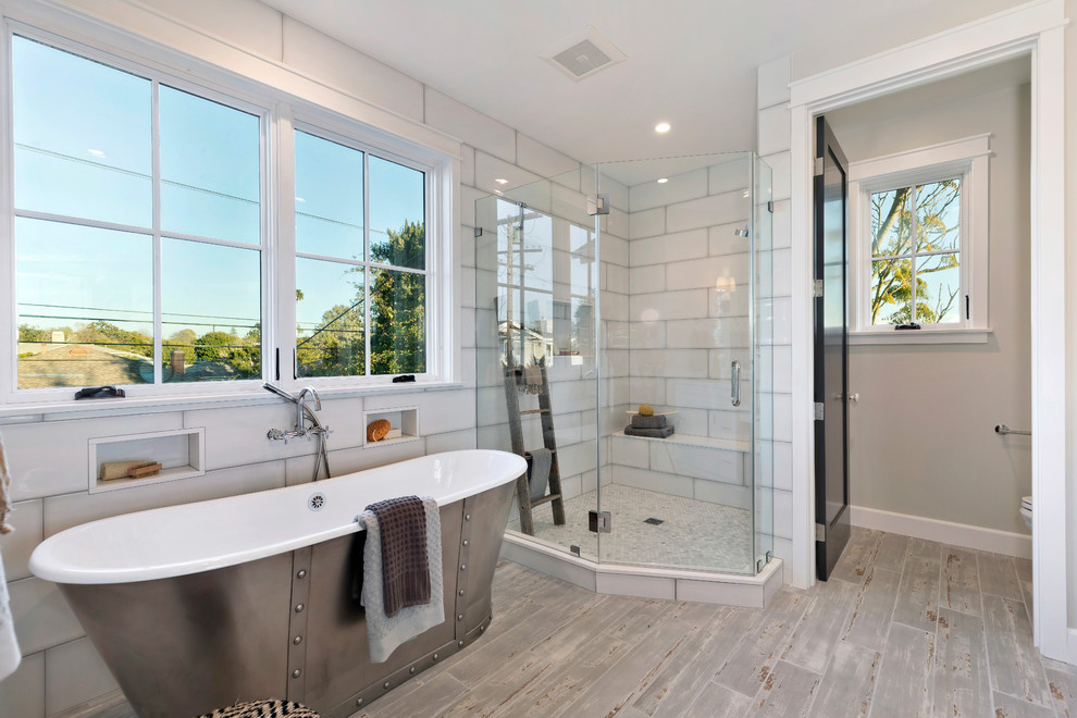 This is an example of a country master bathroom in Los Angeles with a freestanding tub, an alcove shower, white tile, grey walls, grey floor, a hinged shower door and a shower seat.