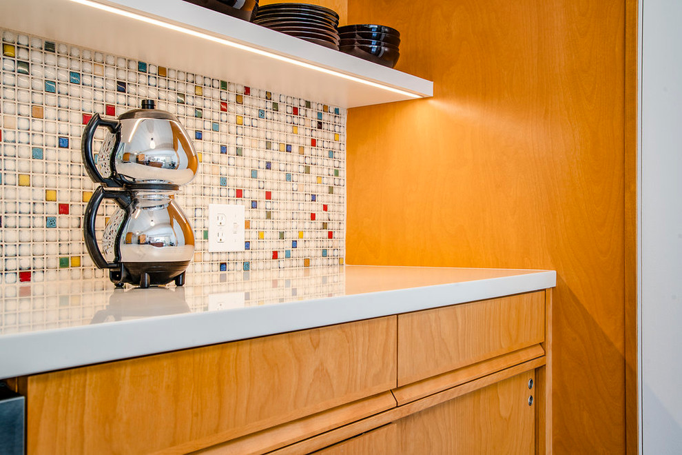 Mid-sized midcentury galley open plan kitchen in Los Angeles with an undermount sink, flat-panel cabinets, multi-coloured splashback, stainless steel appliances, a peninsula, black floor, white benchtop, medium wood cabinets, solid surface benchtops, mosaic tile splashback and slate floors.