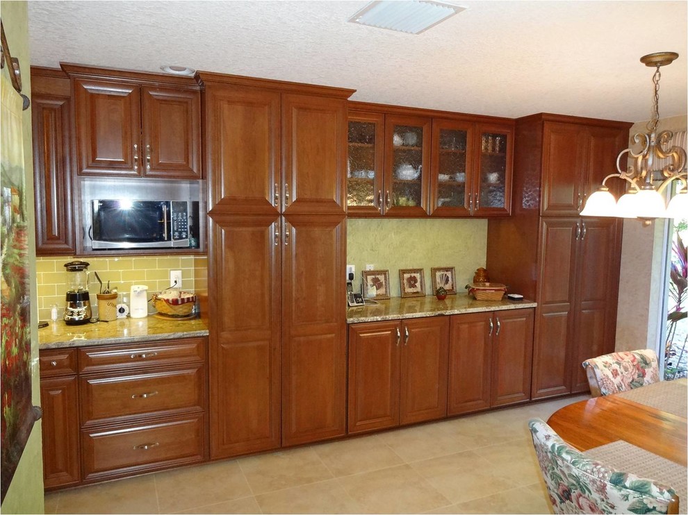 Photo of a large traditional galley eat-in kitchen in Tampa with a double-bowl sink, medium wood cabinets, granite benchtops, glass tile splashback, white appliances, raised-panel cabinets, green splashback, porcelain floors, no island and beige floor.