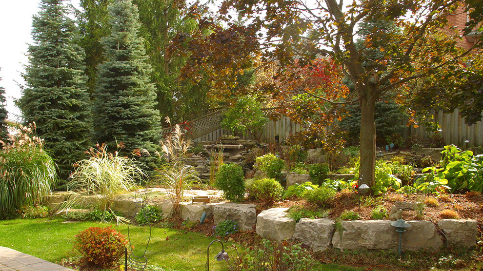 Mid-sized traditional sloped partial sun garden in Toronto with a retaining wall and concrete pavers for fall.