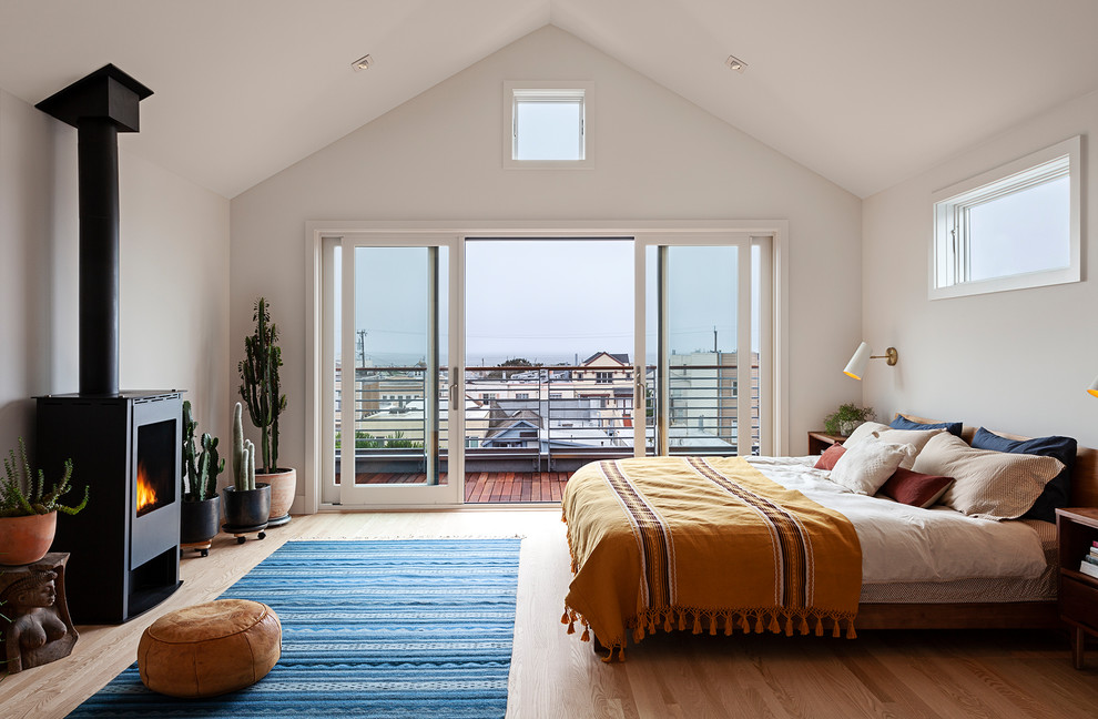 Photo of a modern master bedroom in San Francisco with white walls, light hardwood floors, a wood stove and a metal fireplace surround.