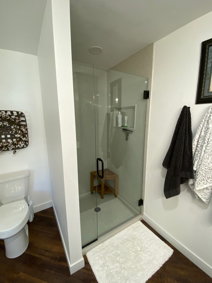 Foto på ett mellanstort funkis en-suite badrum, med en dusch i en alkov, en toalettstol med separat cisternkåpa, laminatgolv, brunt golv och dusch med gångjärnsdörr