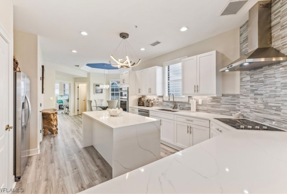 This is an example of a mid-sized beach style l-shaped eat-in kitchen in Miami with an undermount sink, shaker cabinets, white cabinets, quartzite benchtops, grey splashback, glass tile splashback, stainless steel appliances, laminate floors, multiple islands, green floor and white benchtop.