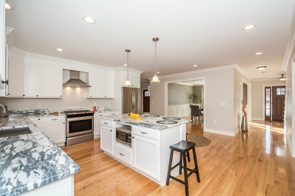 Large transitional l-shaped brown floor and medium tone wood floor eat-in kitchen photo in Boston with an undermount sink, recessed-panel cabinets, white cabinets, stone slab backsplash, stainless steel appliances, an island and quartzite countertops