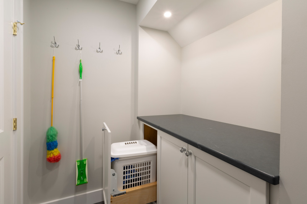 Photo of a medium sized traditional l-shaped separated utility room in New York with a submerged sink, shaker cabinets, white cabinets, engineered stone countertops, multi-coloured splashback, mosaic tiled splashback, beige walls, a stacked washer and dryer and black worktops.