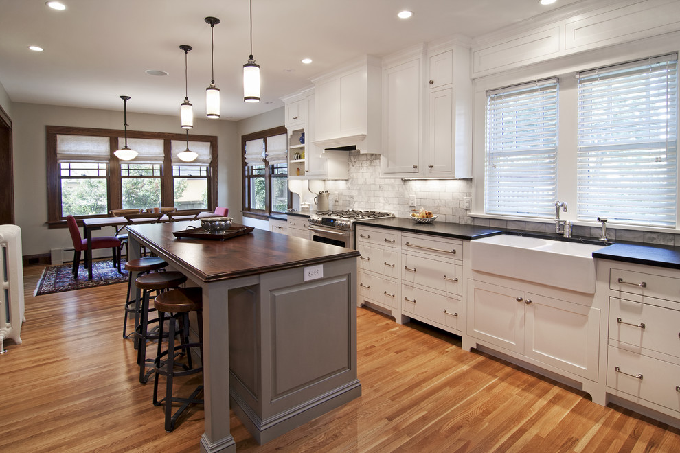 This is an example of a country eat-in kitchen in Minneapolis with a farmhouse sink, wood benchtops, white splashback and stone tile splashback.