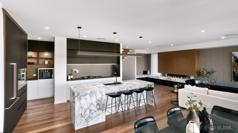 Photo of an expansive contemporary open plan kitchen in Brisbane with an undermount sink, flat-panel cabinets, black cabinets, marble benchtops, black splashback, stone slab splashback, black appliances, medium hardwood floors, with island, brown floor and white benchtop.