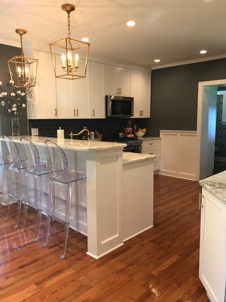 This is an example of a mid-sized transitional l-shaped kitchen in Philadelphia with an undermount sink, recessed-panel cabinets, white cabinets, quartzite benchtops, grey splashback, glass tile splashback, stainless steel appliances, light hardwood floors, a peninsula and brown floor.