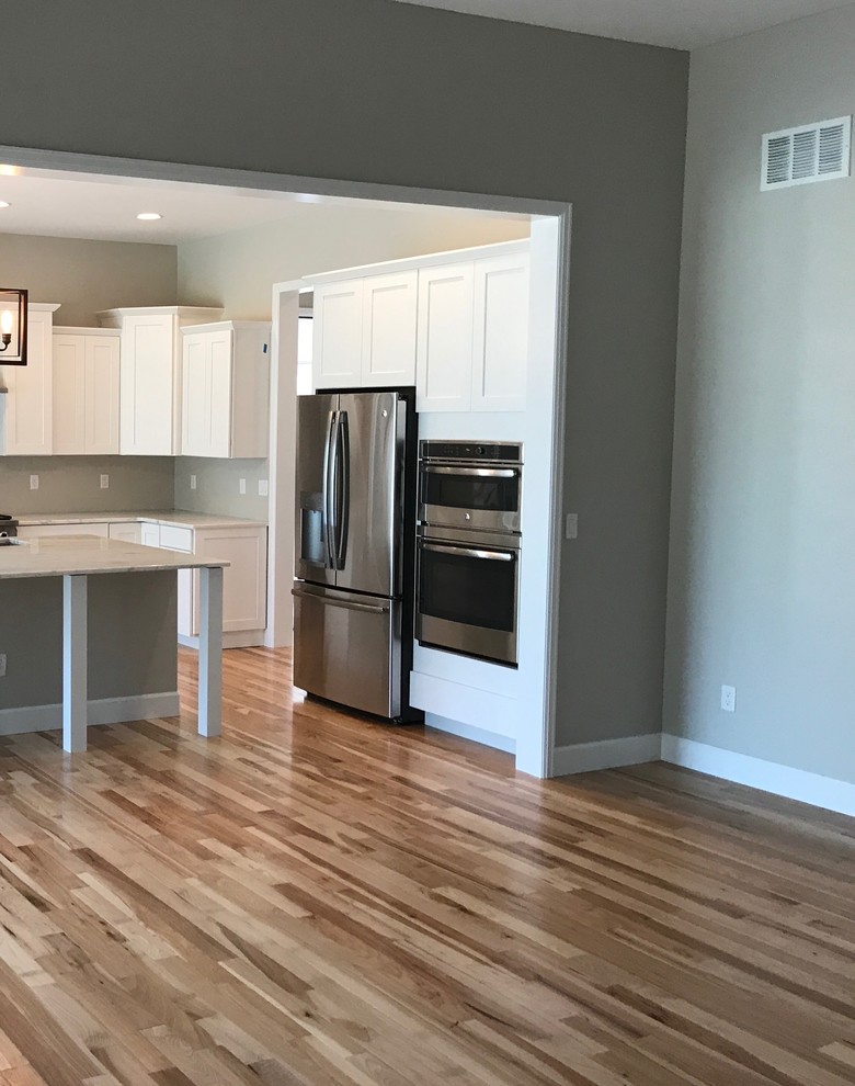 Example of a mid-sized transitional l-shaped medium tone wood floor and brown floor open concept kitchen design in Denver with shaker cabinets, white cabinets, marble countertops, stainless steel appliances, an island and gray countertops