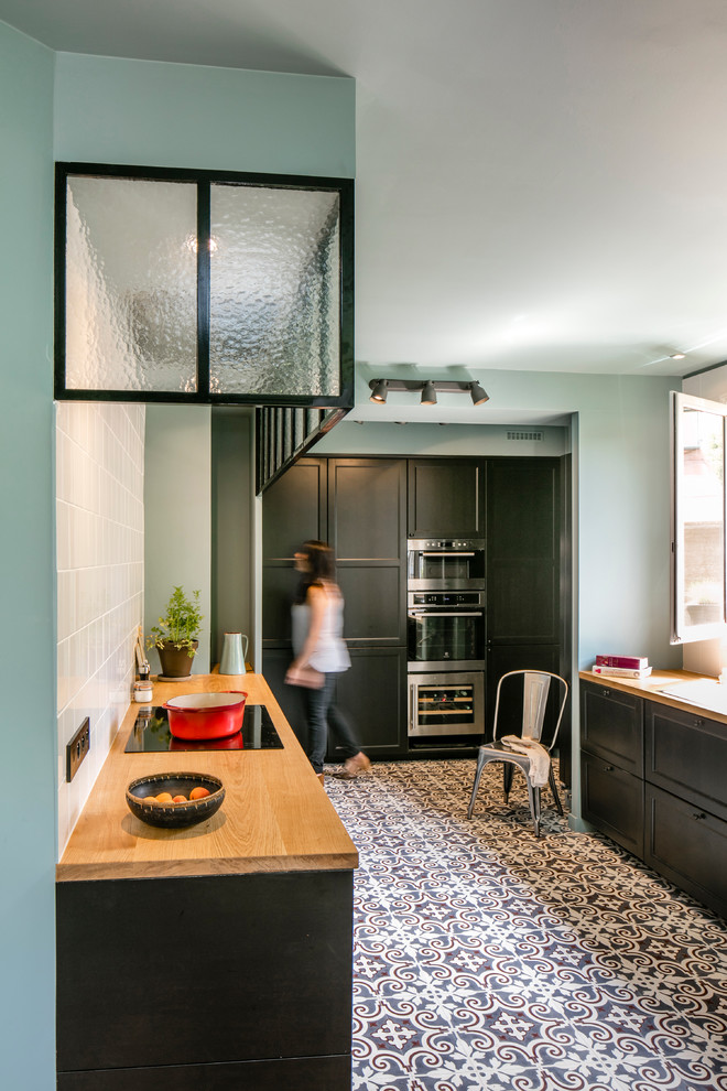 This is an example of a mid-sized contemporary galley kitchen in Paris with black cabinets, wood benchtops, white splashback, matchstick tile splashback, ceramic floors and beige benchtop.
