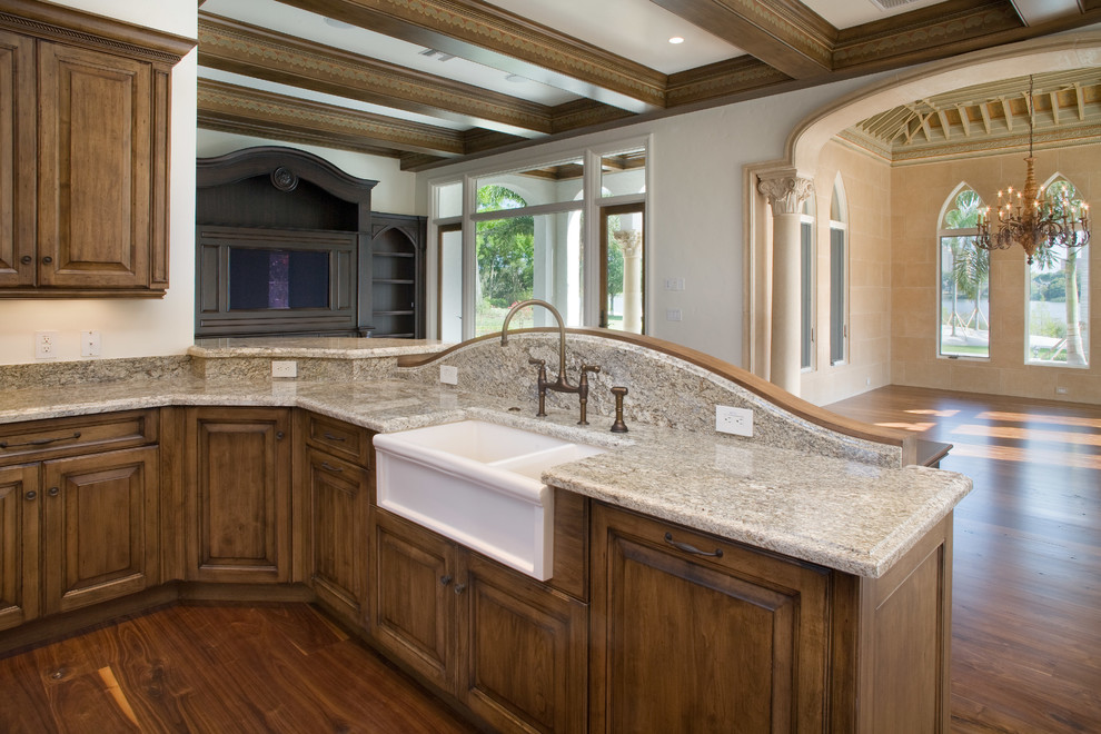 Huge elegant u-shaped medium tone wood floor open concept kitchen photo in Orlando with raised-panel cabinets, dark wood cabinets, granite countertops, beige backsplash, stone slab backsplash, an island, a farmhouse sink and paneled appliances
