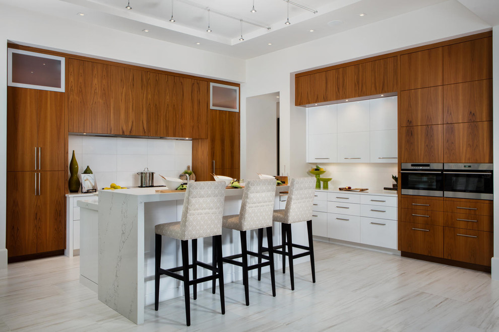 Contemporary kitchen with flat-panel cabinets, white splashback, stainless steel appliances, with island and beige floor.