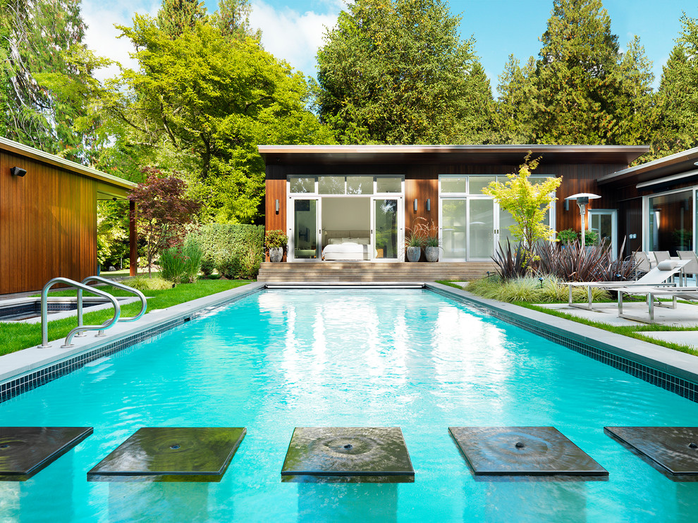 Photo of a mid-sized midcentury backyard rectangular lap pool in Vancouver with a pool house and concrete pavers.