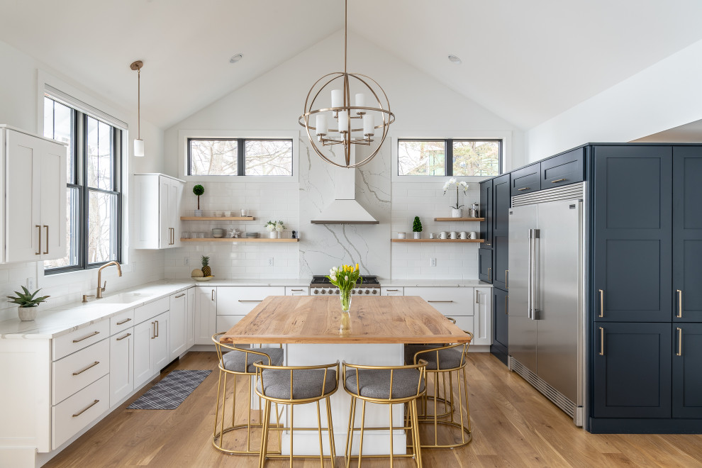 Large transitional u-shaped kitchen in Other with an undermount sink, white cabinets, quartz benchtops, white splashback, stainless steel appliances, medium hardwood floors, with island, brown floor, white benchtop and shaker cabinets.