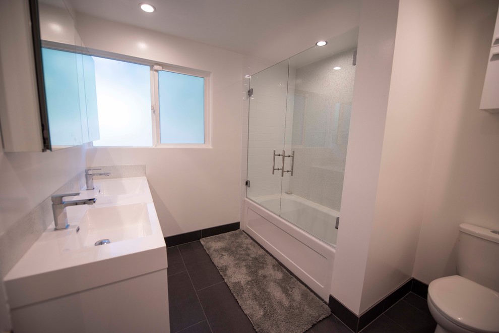 Photo of a small modern kids bathroom in Other with furniture-like cabinets, white cabinets, an alcove tub, a two-piece toilet, white tile, glass sheet wall, white walls, porcelain floors, an integrated sink, black floor and white benchtops.