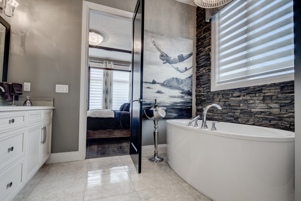This is an example of a large contemporary master bathroom in Edmonton with an undermount sink, white cabinets, engineered quartz benchtops, a freestanding tub, a one-piece toilet, beige tile, ceramic tile, grey walls and ceramic floors.