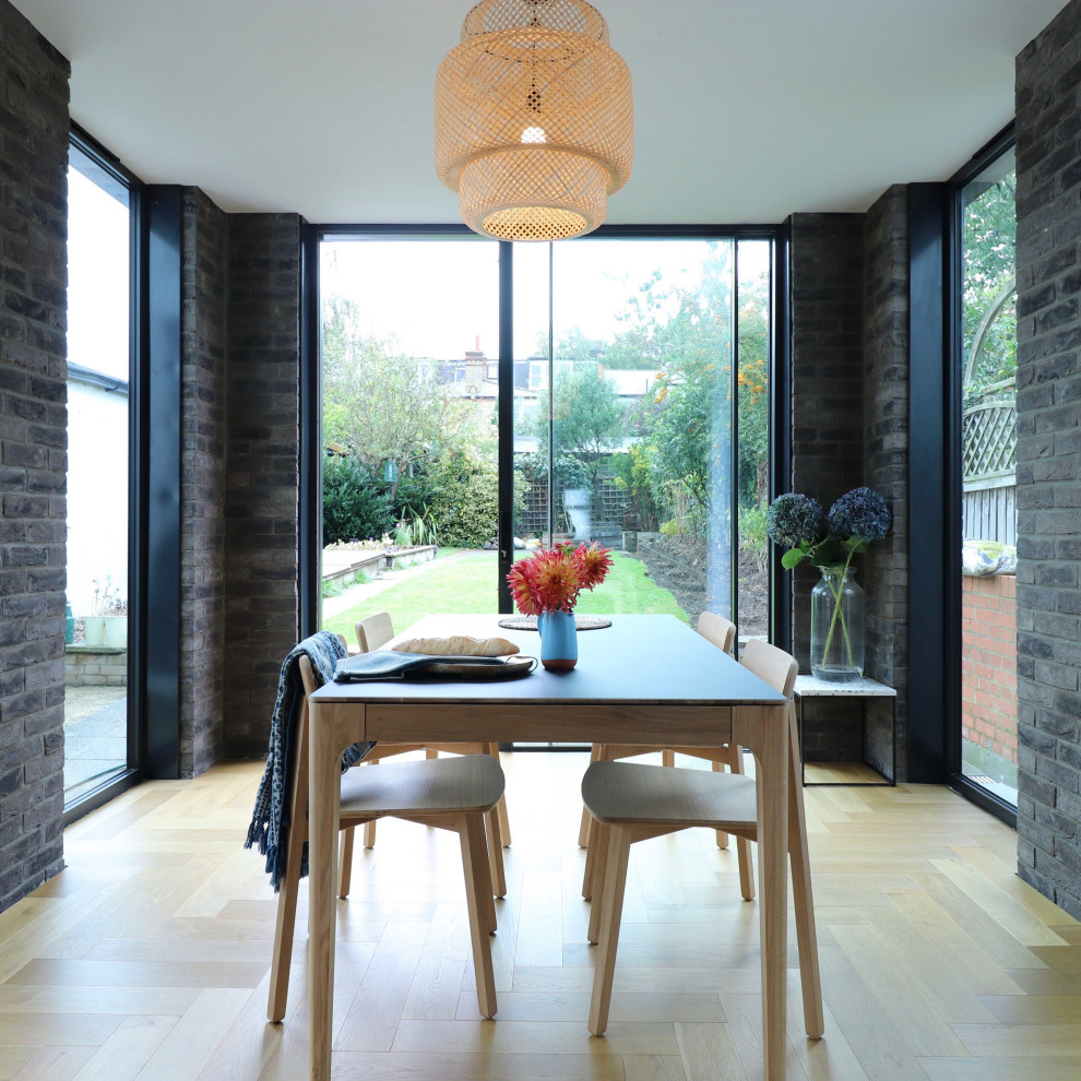 Example of a mid-sized trendy brick wall, light wood floor and beige floor dining room design in London with gray walls