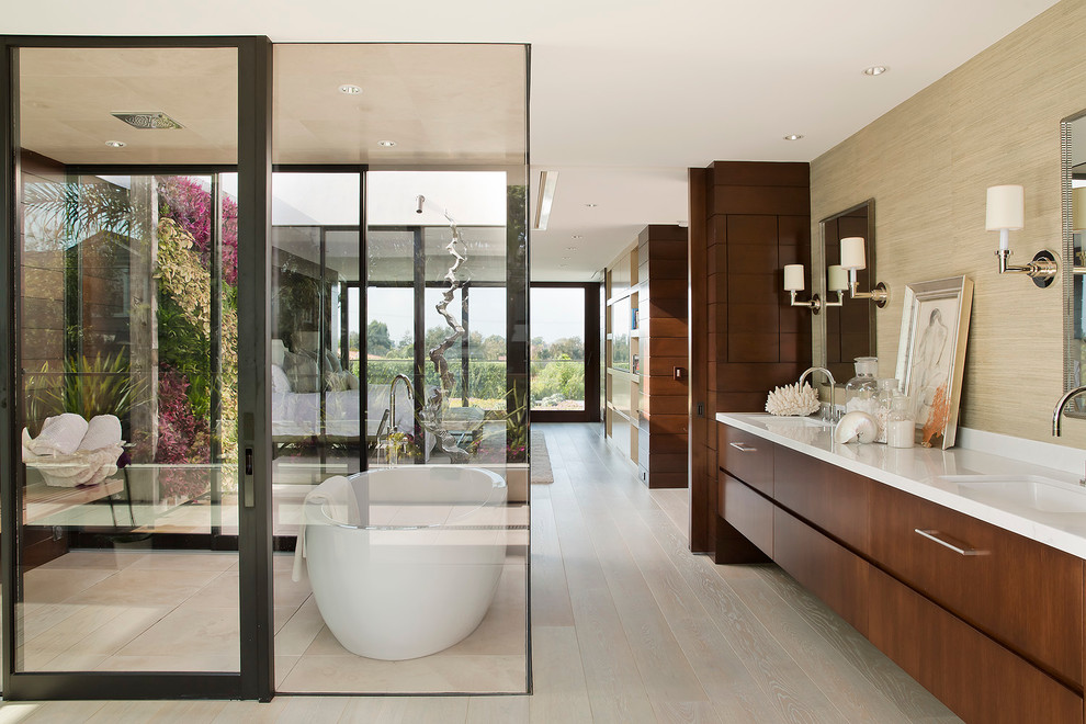 Expansive contemporary master bathroom in Los Angeles with flat-panel cabinets, dark wood cabinets, a freestanding tub, beige tile, stone tile, brown walls, light hardwood floors, an undermount sink and marble benchtops.