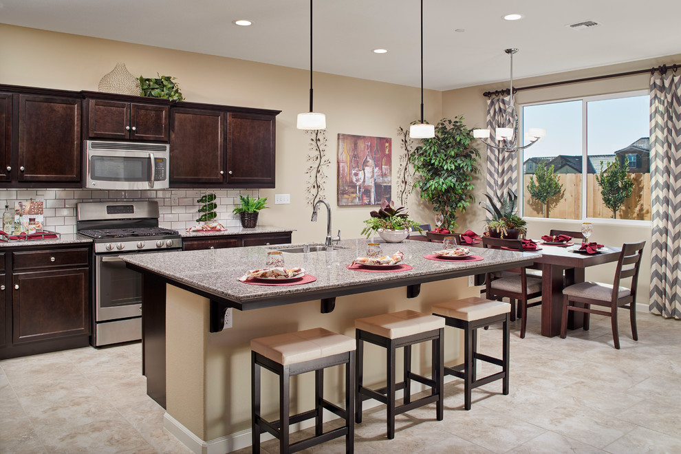 Inspiration for a transitional kitchen remodel with a drop-in sink, dark wood cabinets, granite countertops, white backsplash, subway tile backsplash, stainless steel appliances and an island
