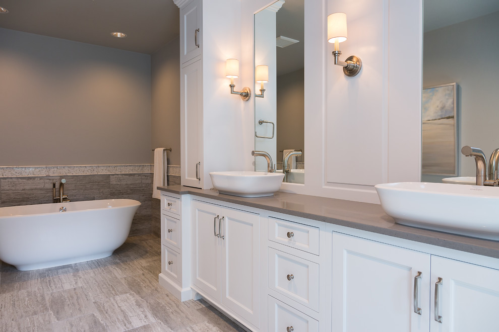 Freestanding bathtub - large transitional beige tile and porcelain tile porcelain tile freestanding bathtub idea with recessed-panel cabinets, gray walls, a vessel sink, solid surface countertops and white cabinets
