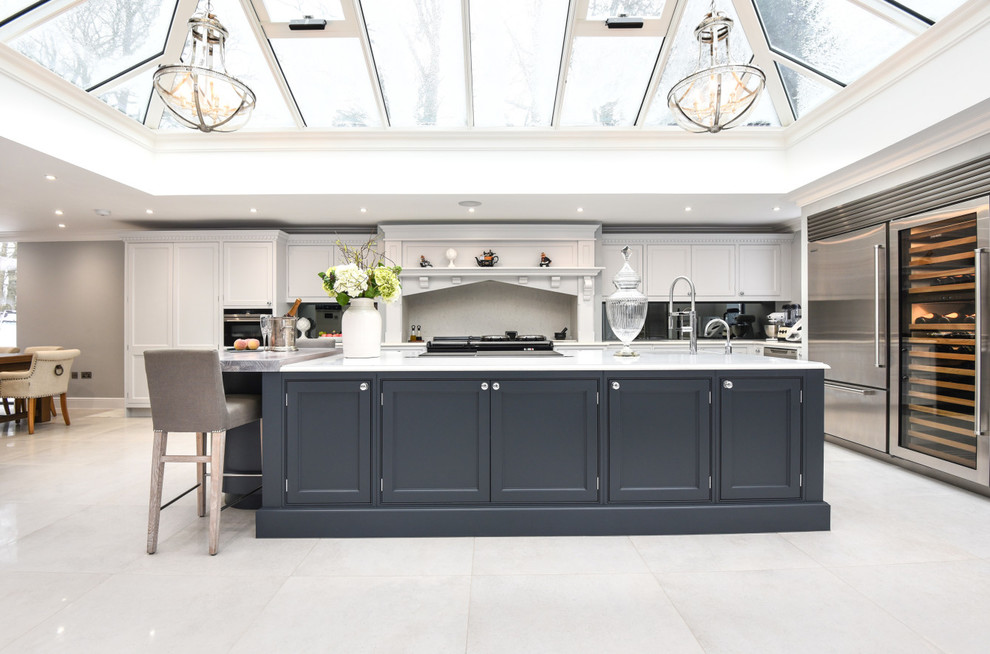 This is an example of a large transitional l-shaped eat-in kitchen in Berkshire with granite benchtops, with island, white benchtop, white floor, recessed-panel cabinets, white cabinets, black splashback, glass sheet splashback and stainless steel appliances.