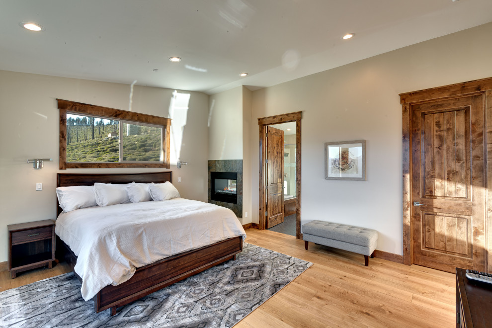 Design ideas for a large transitional master bedroom in Other with beige walls, light hardwood floors, a two-sided fireplace, a tile fireplace surround and vaulted.
