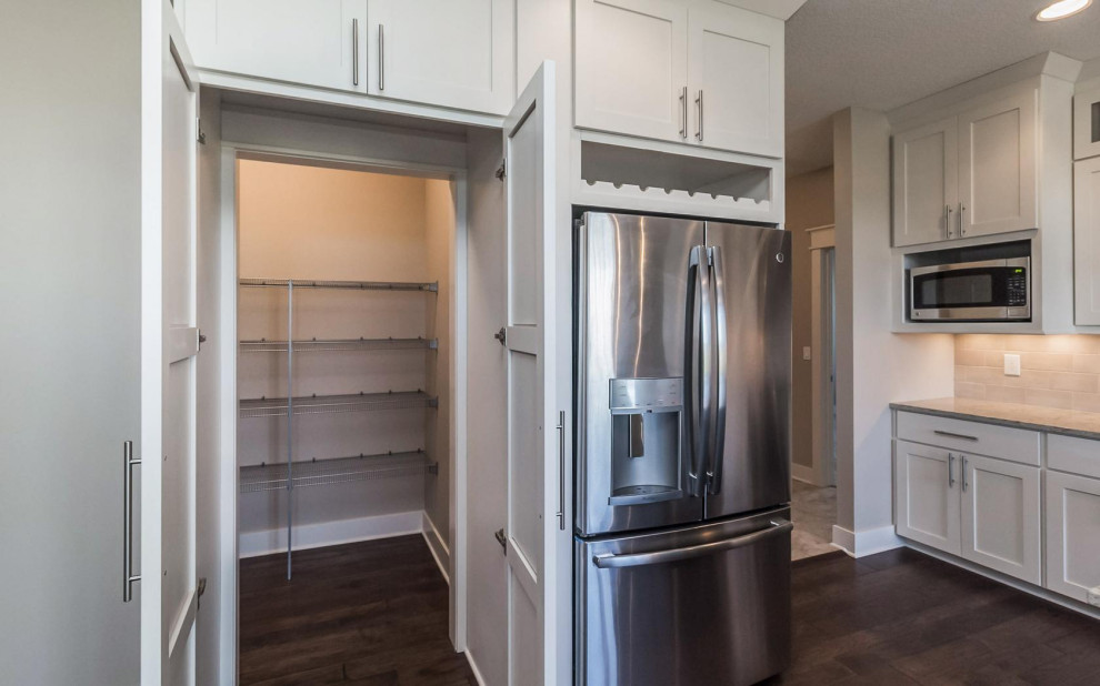 Inspiration for a transitional l-shaped medium tone wood floor and brown floor eat-in kitchen remodel with an undermount sink, shaker cabinets, white cabinets, quartz countertops, ceramic backsplash, stainless steel appliances and an island