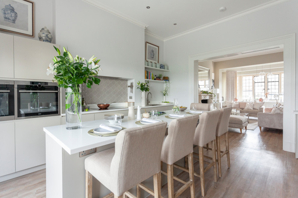 Large contemporary open plan kitchen in Other with a drop-in sink, flat-panel cabinets, beige cabinets, solid surface benchtops, grey splashback, ceramic splashback, stainless steel appliances, with island and white benchtop.