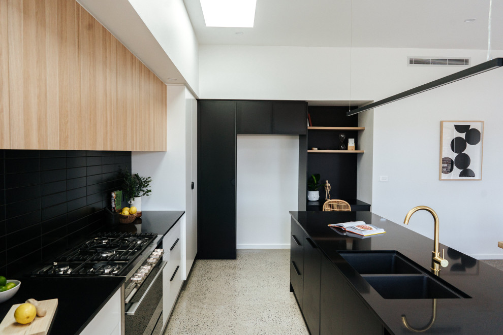 Photo of a mid-sized modern galley open plan kitchen in Wollongong with an undermount sink, flat-panel cabinets, black cabinets, quartz benchtops, black splashback, ceramic splashback, stainless steel appliances, concrete floors, with island, grey floor and black benchtop.