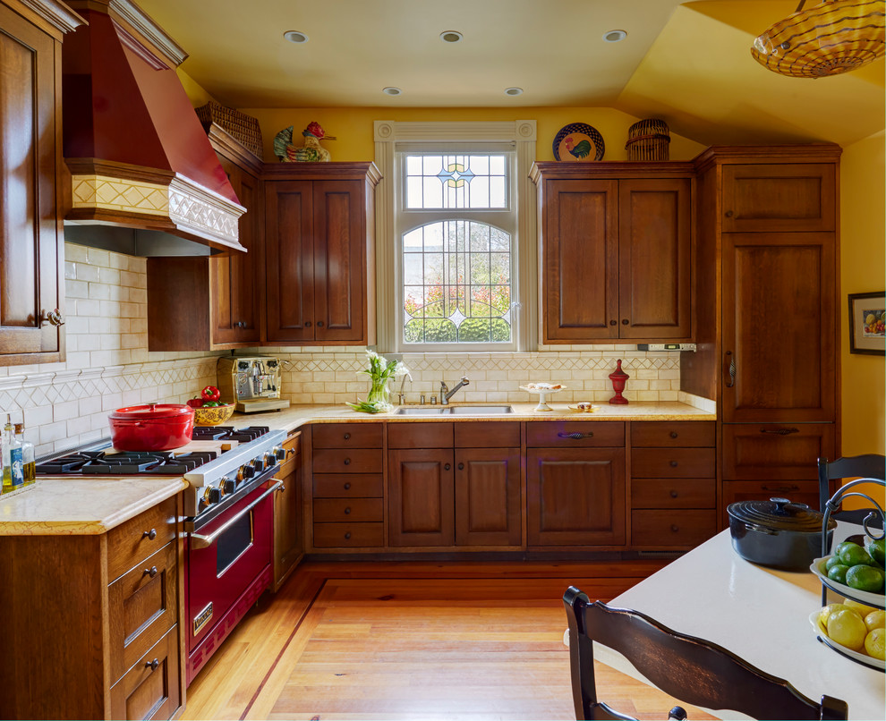 Photo of a mid-sized traditional l-shaped eat-in kitchen in San Francisco with a double-bowl sink, raised-panel cabinets, marble benchtops, white splashback, ceramic splashback, coloured appliances, medium hardwood floors, no island, medium wood cabinets and orange floor.