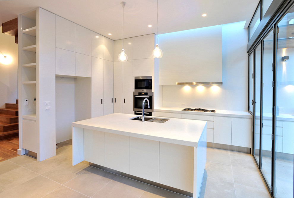 Photo of a mid-sized contemporary l-shaped kitchen pantry in Melbourne with an undermount sink, flat-panel cabinets, white cabinets, quartz benchtops, white splashback, glass sheet splashback, stainless steel appliances, ceramic floors and with island.
